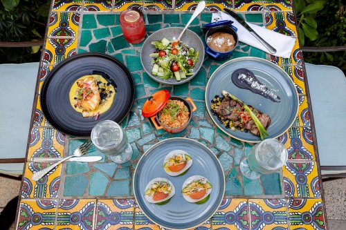 A colorful table set with various dishes, including seafood, salad, and steak, surrounded by vibrant tile patterns.