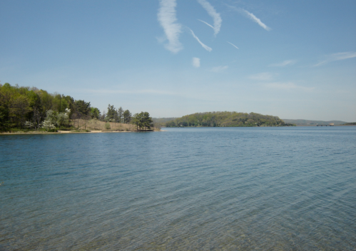 A serene lake surrounded by green hills and a clear blue sky, with gentle ripples on the water's surface.