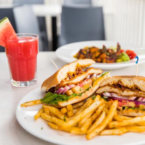 A close-up of a sandwich with fries and a watermelon drink in the background, showcasing vibrant colors and textures.