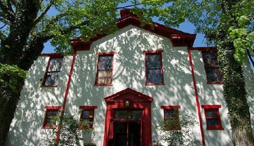 A white building with red trim, surrounded by trees, casting shadows on its facade under a clear blue sky.