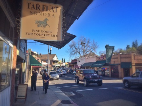 A street view of Sonora, California, featuring shops, a sign for Tar Flat, and a parked Jeep under a clear blue sky.