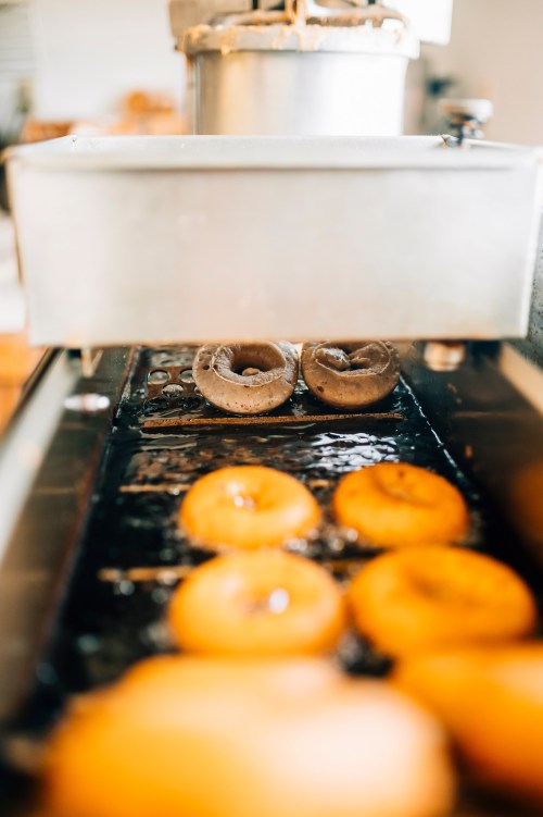 Freshly fried donuts on a conveyor belt, with golden and chocolate varieties emerging from the fryer.