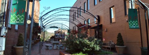 A charming courtyard with arches, greenery, and seating, surrounded by brick buildings under a clear blue sky.
