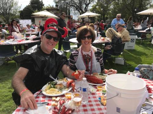 A couple enjoying a seafood feast at an outdoor event, wearing festive attire and surrounded by tables and guests.