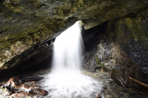 A waterfall cascades over rocks, flowing into a serene pool beneath a rocky overhang.