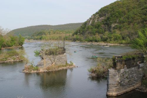 A serene river scene with lush green hills, featuring remnants of a stone structure and kayakers in the water.