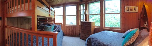 Cozy wooden bedroom with a bunk bed, a double bed, and large windows overlooking greenery.