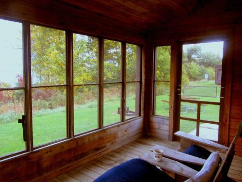 Cozy wooden porch with large windows, a chair, and a view of a green yard and trees outside.
