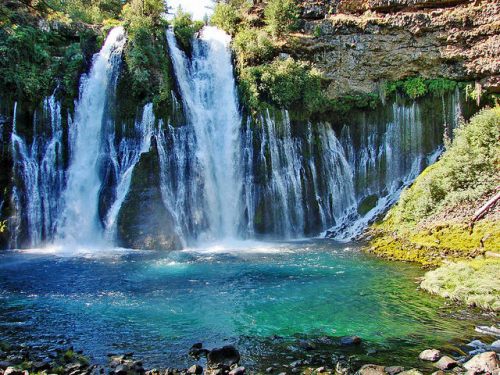 A scenic waterfall cascading into a clear blue pool, surrounded by lush greenery and rocky cliffs.