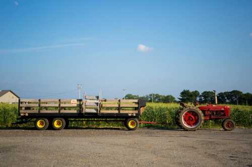 A red tractor pulls a wooden wagon beside a field under a clear blue sky.