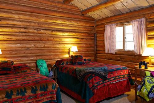 Cozy log cabin bedroom with two beds, colorful blankets, and warm lighting from bedside lamps.