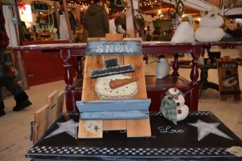 A rustic display featuring a snowman decoration and a sign that says "Let It Snow" on a wooden table.