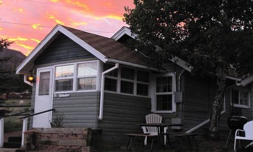 A cozy gray cottage with a porch, surrounded by trees, under a vibrant sunset sky.