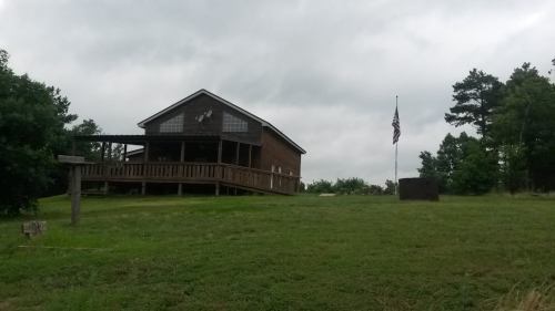 A wooden house on a grassy hill, with an American flag and cloudy sky in the background.