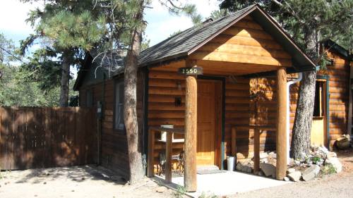 A rustic log cabin with a wooden porch, surrounded by trees and a gravel path.