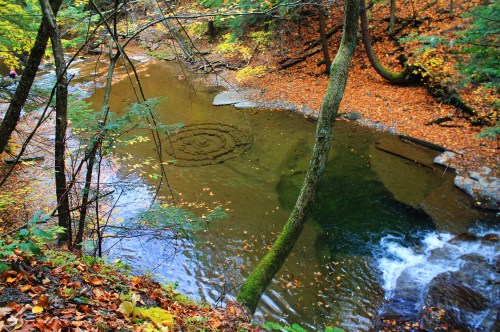A serene river surrounded by autumn foliage, with a circular pattern visible in the water.