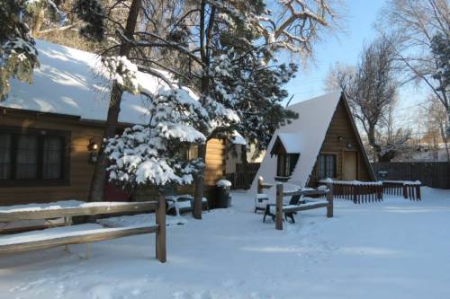 Two cozy cabins surrounded by snow-covered trees, with a picnic table in a winter landscape.
