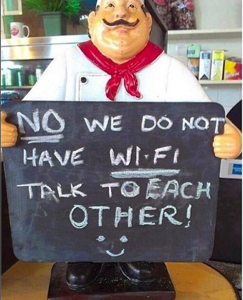 A cheerful chef statue holding a sign that says, "No, we do not have Wi-Fi. Talk to each other!" with a smiley face.