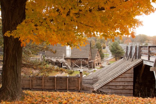 A scenic view of a historic mill surrounded by autumn foliage and wooden structures.