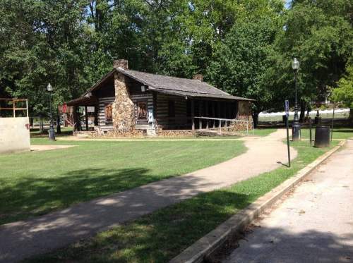 A rustic log cabin surrounded by trees and a grassy area, with a pathway leading to it.