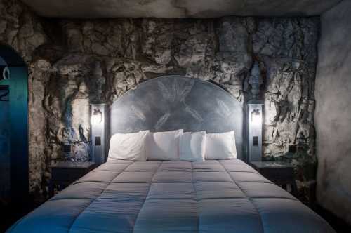 A cozy bedroom featuring a stone wall, a large bed with white pillows, and stylish bedside lamps.