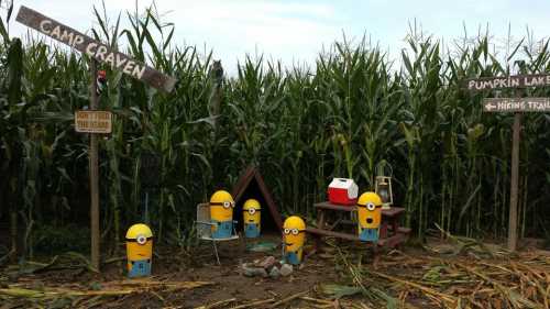 A whimsical scene with Minion figures at a campsite in a cornfield, featuring signs for Camp Craven and Pumpkin Lake.