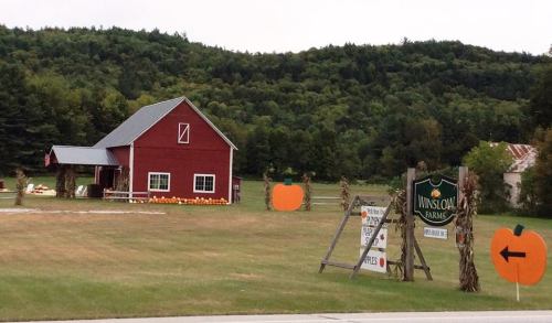 A red barn surrounded by pumpkins and autumn scenery, with a sign for "Janscom Farms" in a rural setting.