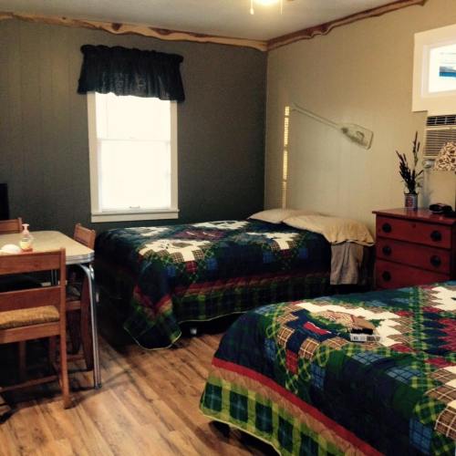 A cozy room with two beds, a table, and a window, featuring simple decor and wooden flooring.