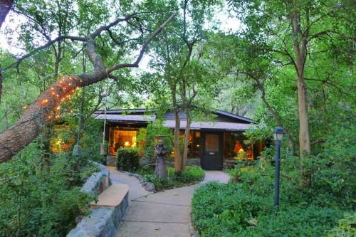 A charming house nestled among lush greenery, with a winding path and warm lights glowing from the windows.