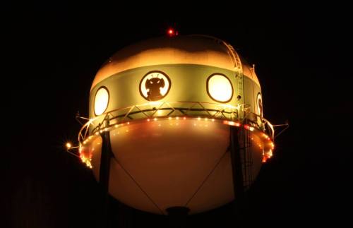 A brightly lit water tower at night, featuring a circular design and decorative lights.