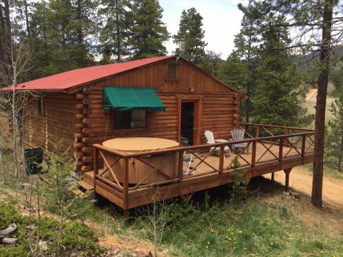 A rustic log cabin with a red roof, surrounded by trees, featuring a deck and hot tub.