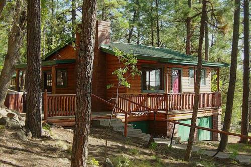 A cozy wooden cabin nestled among tall trees, featuring a wraparound porch and a sloped driveway.