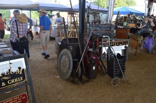 A bustling market scene with various vintage items, signs, and people browsing under tents.