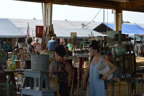 A bustling market scene with people browsing vintage items and antiques under a large tent.