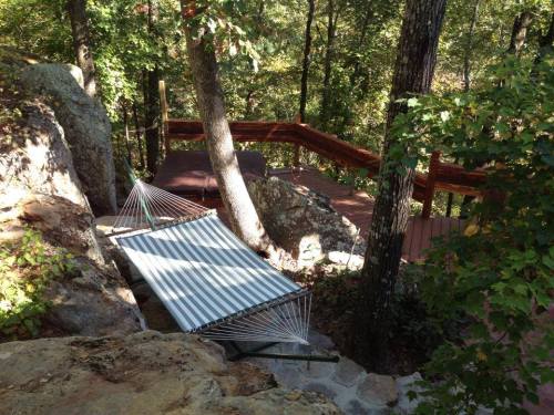 A hammock is nestled between trees on a rocky hillside, with a wooden path winding through the surrounding greenery.