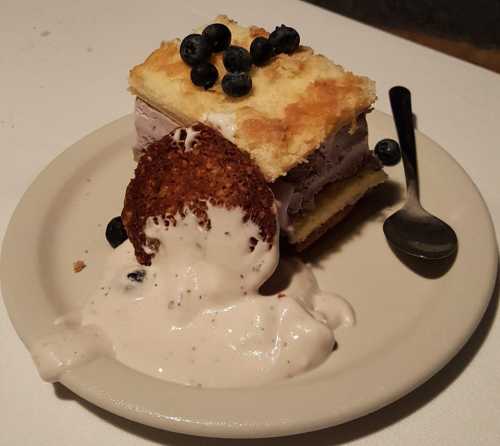 A slice of layered dessert with ice cream, cake, and blueberries, served on a plate with a spoon.