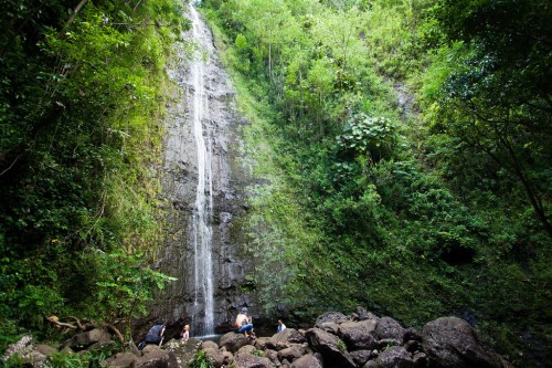 A serene waterfall cascades down a rocky cliff, surrounded by lush greenery and people enjoying the natural beauty below.