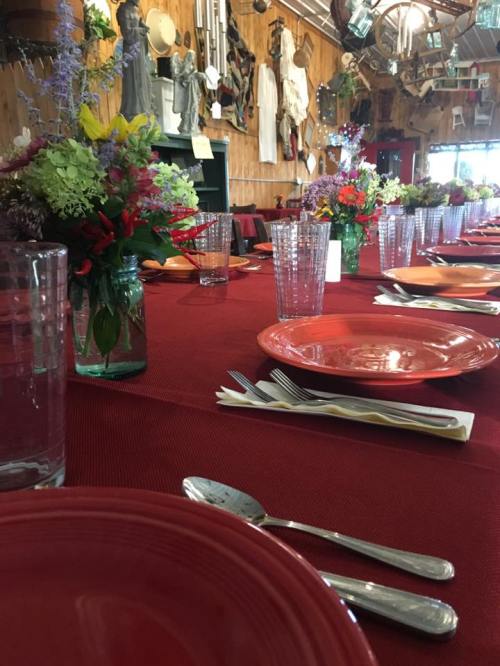 A long dining table set with colorful plates and flowers, surrounded by rustic decor and wooden walls.