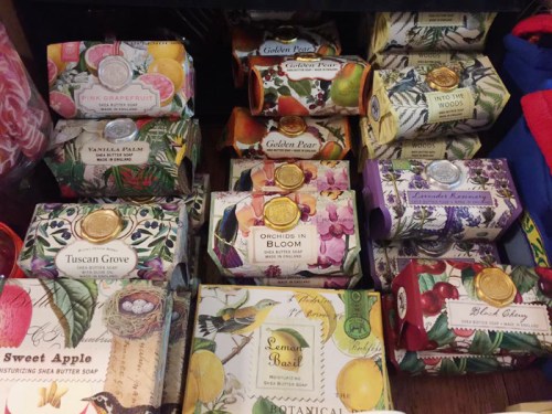 A colorful display of various scented soap bars in decorative packaging, arranged neatly on a shelf.