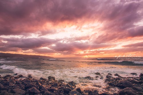 A serene seascape at sunset, with waves crashing against rocky shore and dramatic clouds in the sky.