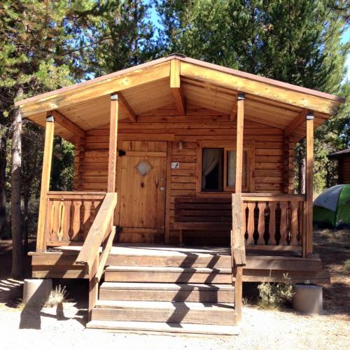 A wooden cabin with a porch and steps, surrounded by trees in a natural setting.