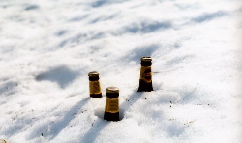 Three beer bottles partially buried in a snowy landscape.