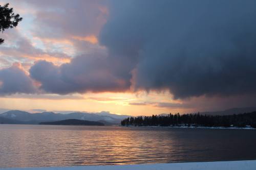 A serene lake at sunset, with dramatic clouds and mountains in the background, reflecting warm colors on the water.