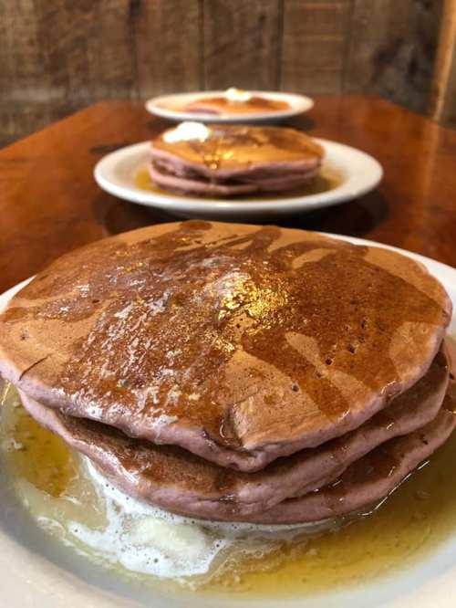 Stack of fluffy pancakes drizzled with syrup, served on a white plate with a wooden background.