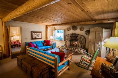 Cozy cabin interior with a stone fireplace, wooden beams, colorful seating, and warm lighting.