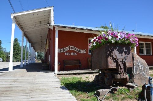 A historic building with a sign reading "Miners Exchange, Est. 1865," featuring a flower planter and wooden walkway.