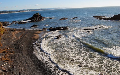 A scenic view of a rocky beach with waves crashing against the shore under a clear blue sky.