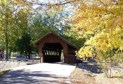 A wooden covered bridge surrounded by vibrant autumn foliage and a clear blue sky.