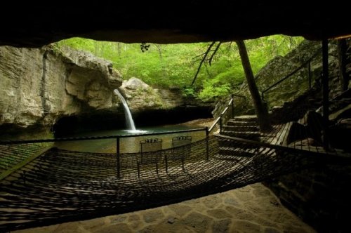 A serene cave interior with a waterfall, surrounded by lush greenery and a hammock near a tranquil pool.