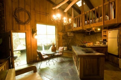 Cozy rustic kitchen with wooden walls, a loft, and a large window overlooking a serene outdoor space.